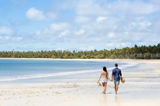 A good-looking Hispanic (Latin) couple walking on a deserted beach with backs to camera, Brazil, South America