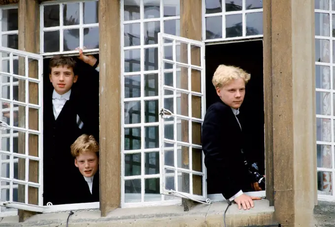 Eton schoolboys in traditional tails looking through the window at Eton College, England, UK