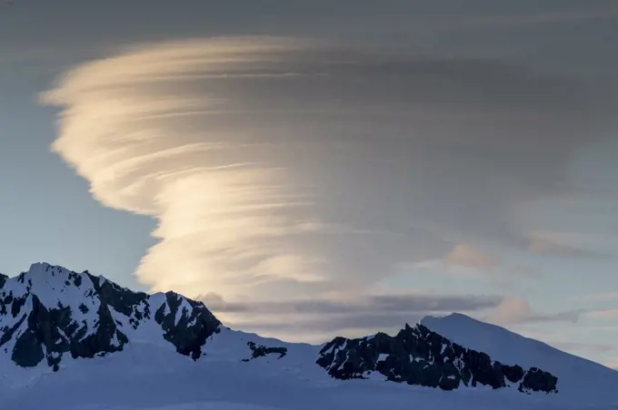Shorefast ice and snow covered mountains with a lenticular cloud build up in Wilhamena Bay, Antarctica, Polar Regions