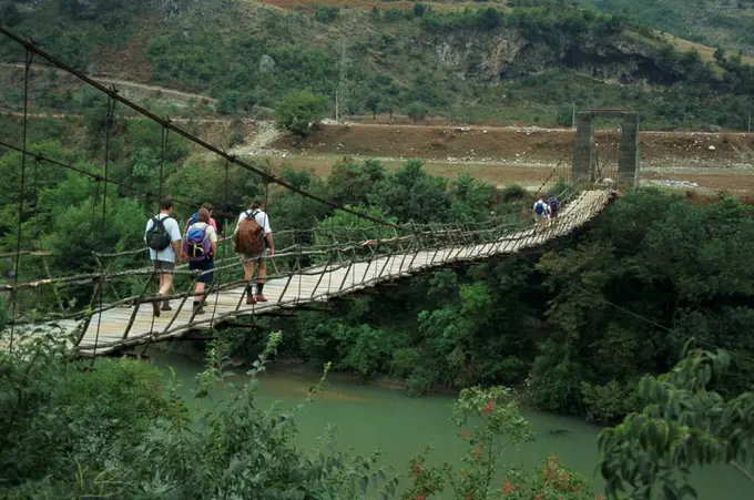 Groups of walkers cross a suspension bridge at Mezhgoran in Albania, Europe