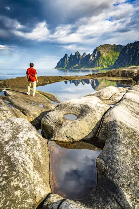 Hiker man contemplating the sharp rocks of mountain peaks standing beside rock pools, Tungeneset, Senja, Troms county, Norway, Scandinavia, Europe