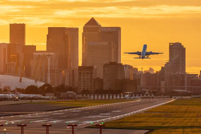 Aircraft taking off from London City Airport at sunset, with Canary Wharf and O2 Arena in background, London, England, United Kingdom, Europe