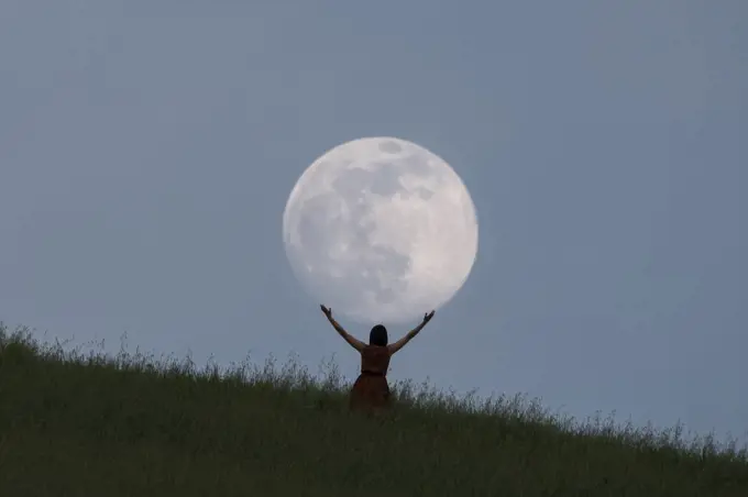 Full moon portrait at blue hour with a girl holding the moon above her head, Emilia Romagna, Italy