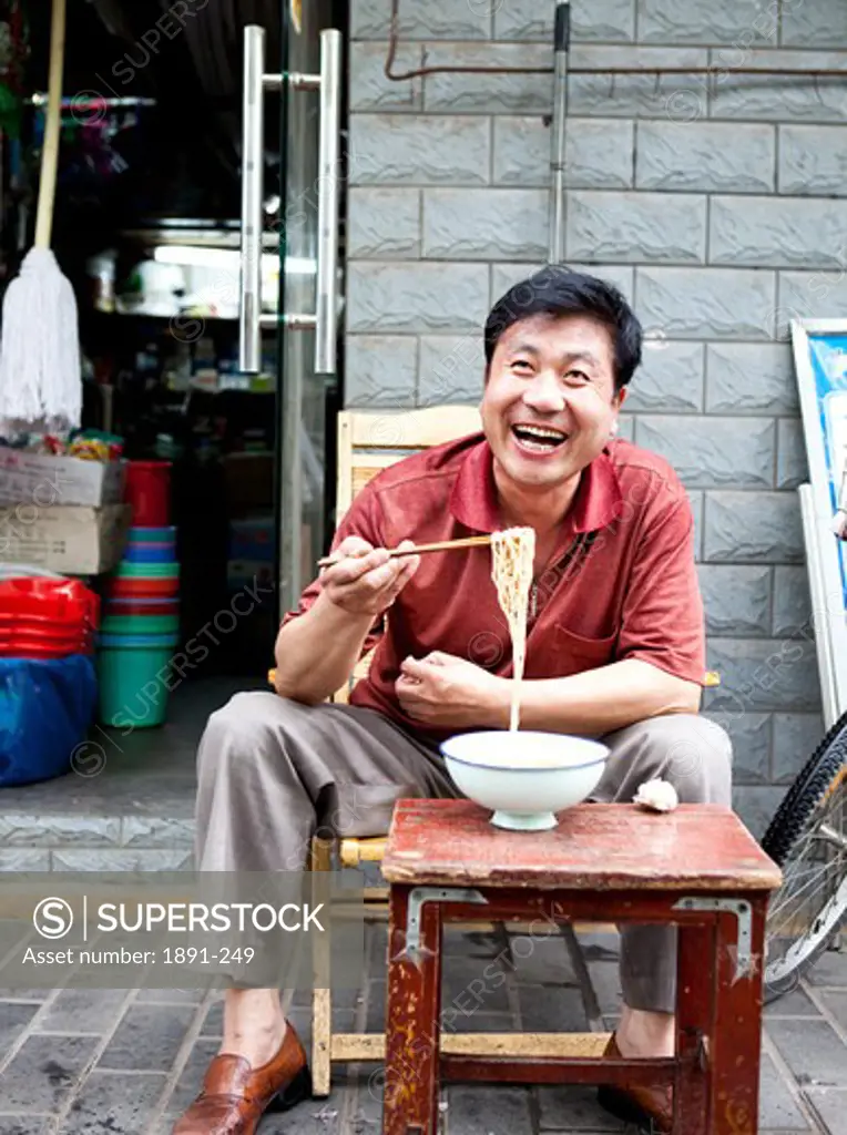 Mature man eating noodles in front of a store, Shanghai, China