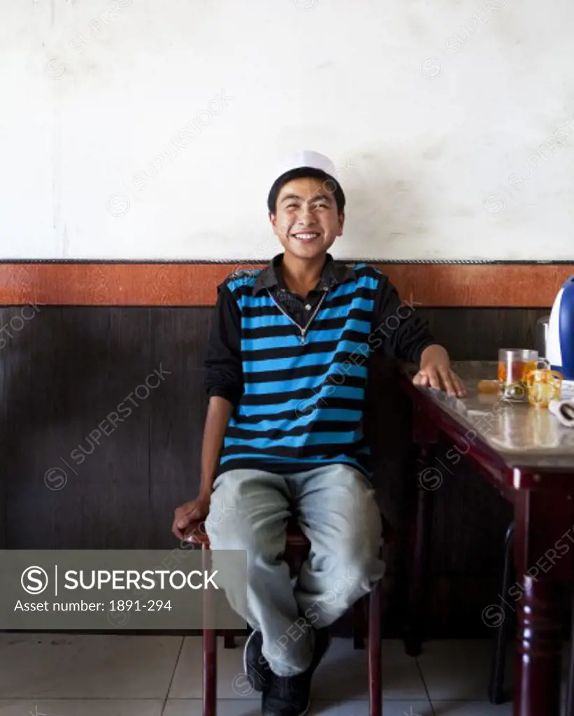Teenage boy sitting on the stool and smiling, Tibet,