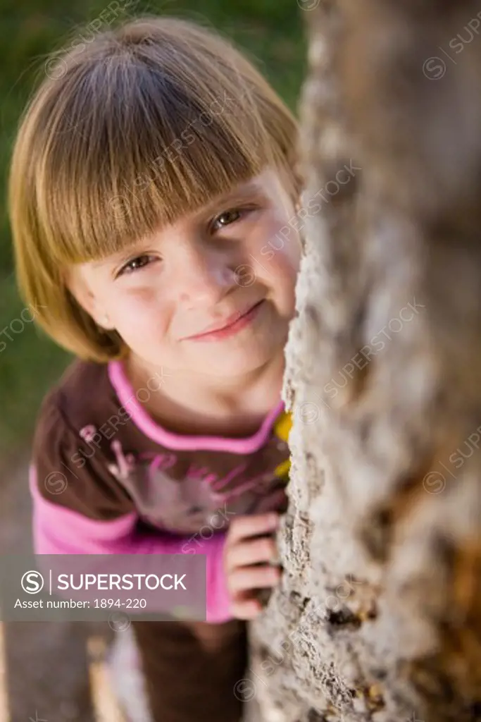 Portrait of a girl peeking from behind a tree