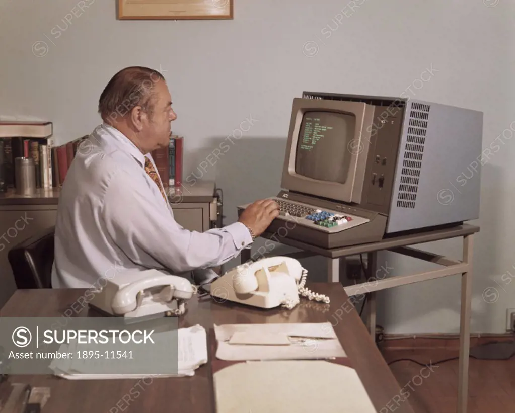 A manager at the international computer firm ICL, consulting a computer record on an early desktop computer in his office in the ICL Headquarters at S...