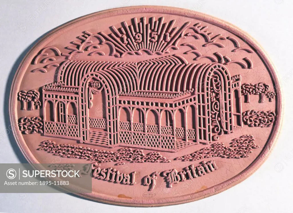 A flat oval pink moulded rubber mat with a raised picture of the Crystal Palace, made by Suba-Maki of England to commemorate the Festival of Britain i...
