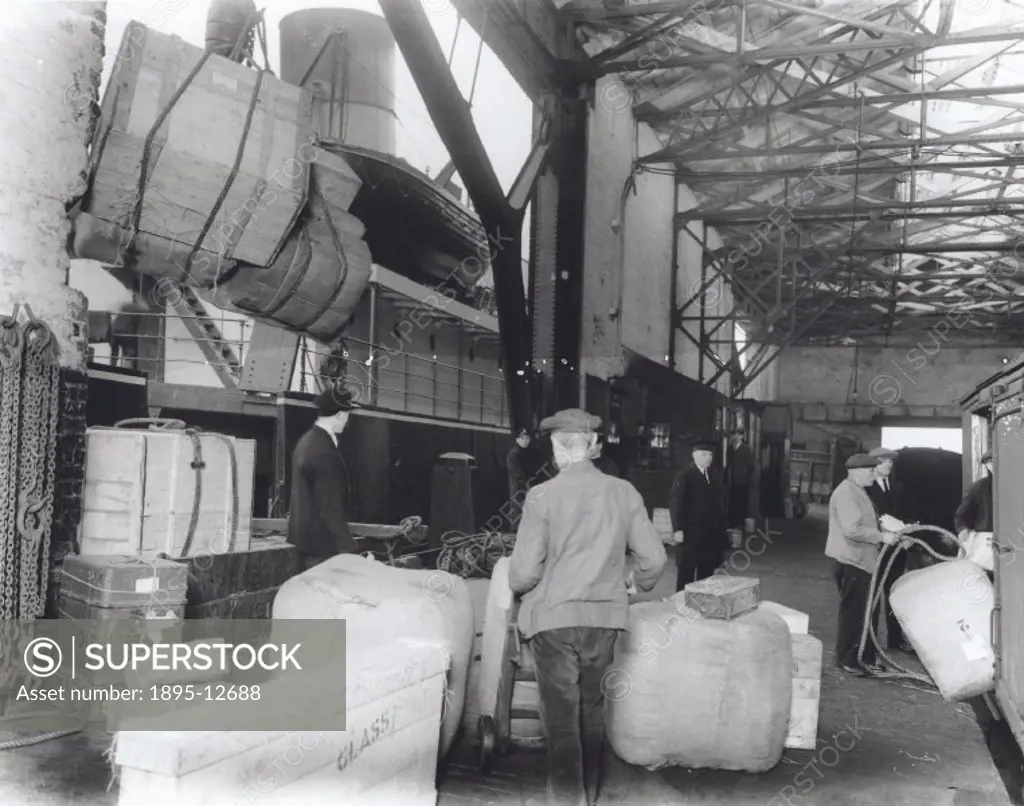Photograph. Dockers at this London, Midland & Scottish Railway´s (LMS) goods depot take the cargo from the railway vans, which is then craned directly...