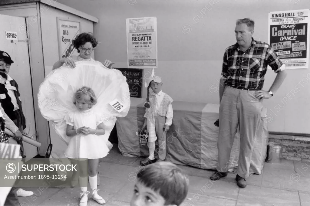 a mother adjusts her daughter´s fancy dress while other children and a bemused man look on. Photograph taken at Herne Bay, Kent. Photographer Tony Ray...