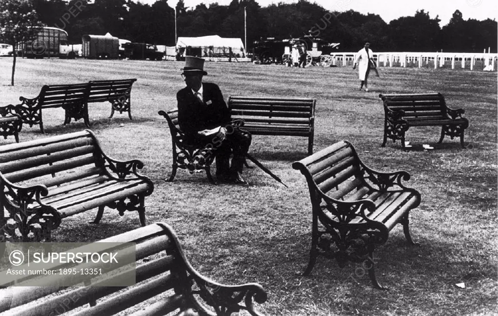 Elderly man in a top hat sitting alone amongst public benches at Ascot horse races, Berkshire. Photographer Tony Ray-Jones (1941-1972) created most of...
