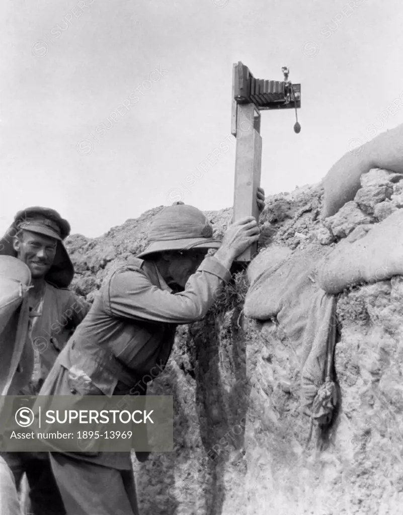 Soldier in a trench taking a photograph with a camera attached to a periscope.