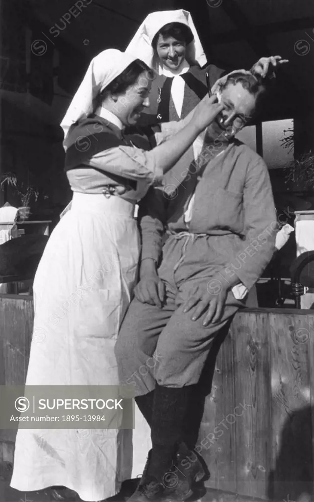 Nurse shaving a soldier with another nurse in close attendance, c 1910s.