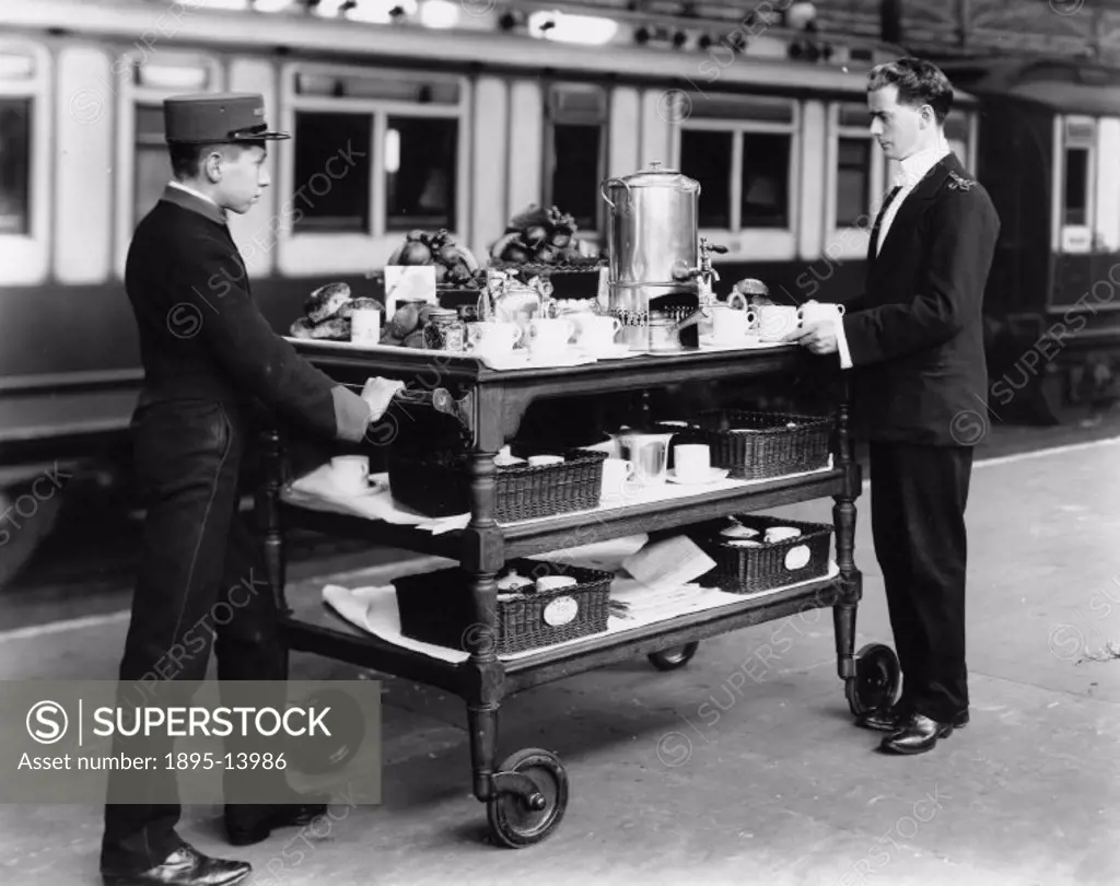 Two London and North Western Railway (LNWR) attendants pose with refreshment trolley on a platform at Euston Station. The trolley is loaded with tea-m...