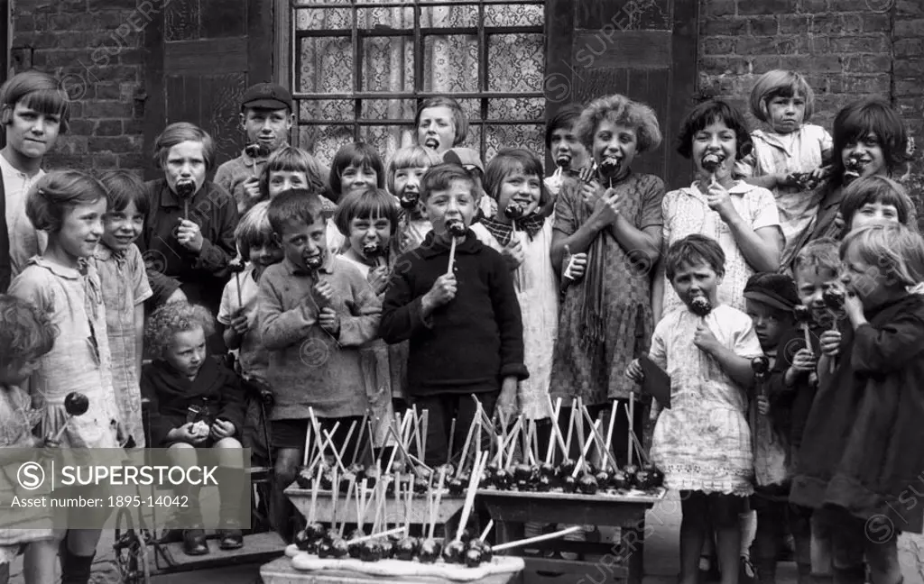 Group of children enjoying toffee apples outside a terraced house. One is sitting in a push-chair.