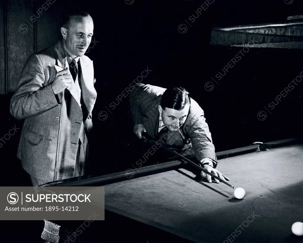 Two men relaxing over a game of billiards, the man smoking on the right is about to strike a ball.