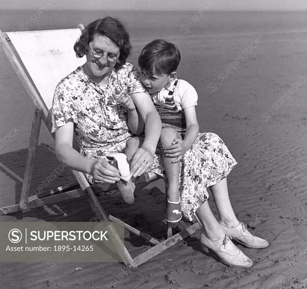 Woman in a deck chair putting a shoe onto her son´s foot, c 1920s