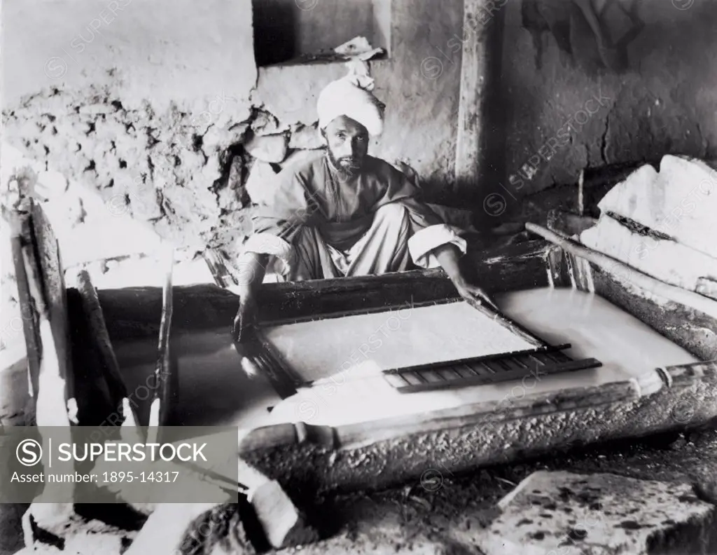 Photograph by W Raitt showing a turbanned craftsman making paper by hand. The pulp is mixed with water and placed on a framed porous screen. The water...
