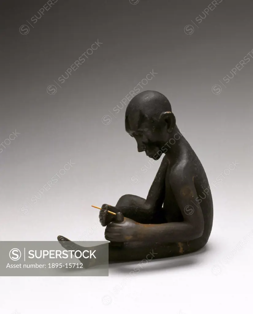 A wooden statue of an East African man removing a sand flea from his foot.