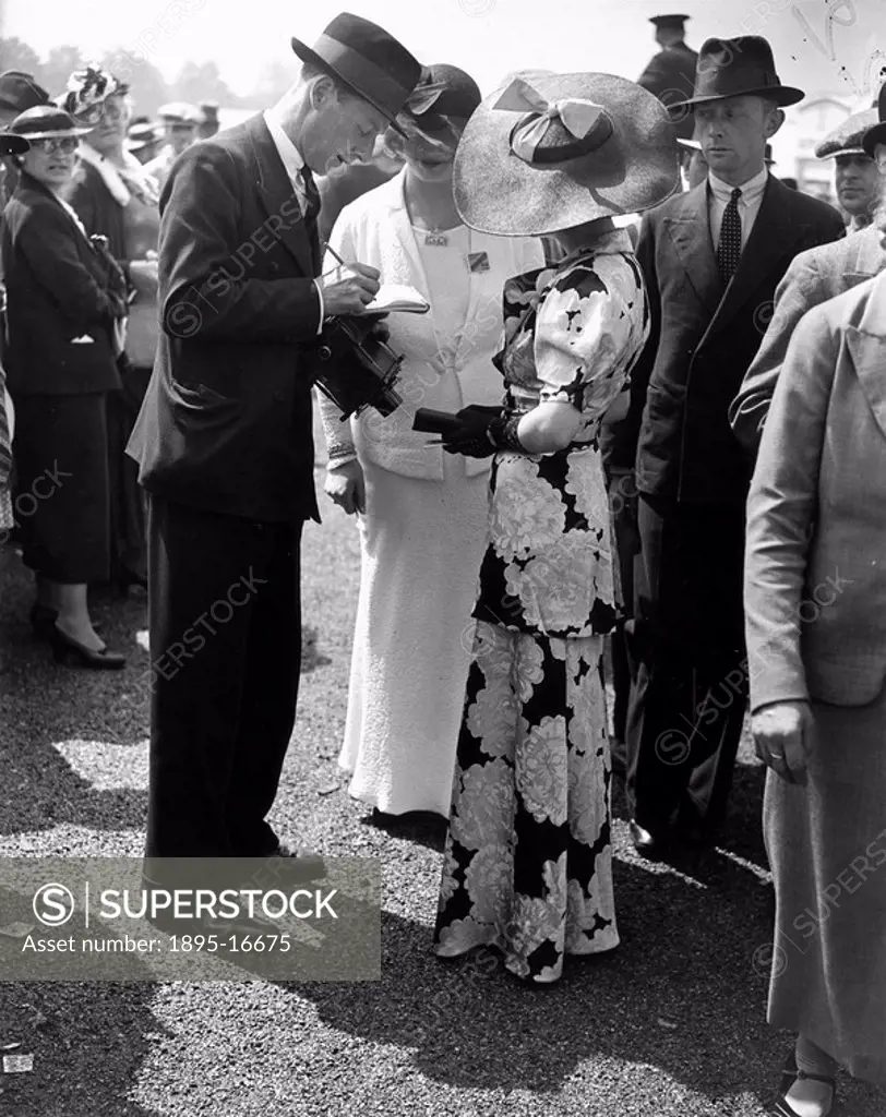 Fashions at the Royal Ascot Races, Berkshire, Gold Cup Day, 18 June 1936. A photographer interviewing two young racegoers wearing the latest summer fa...