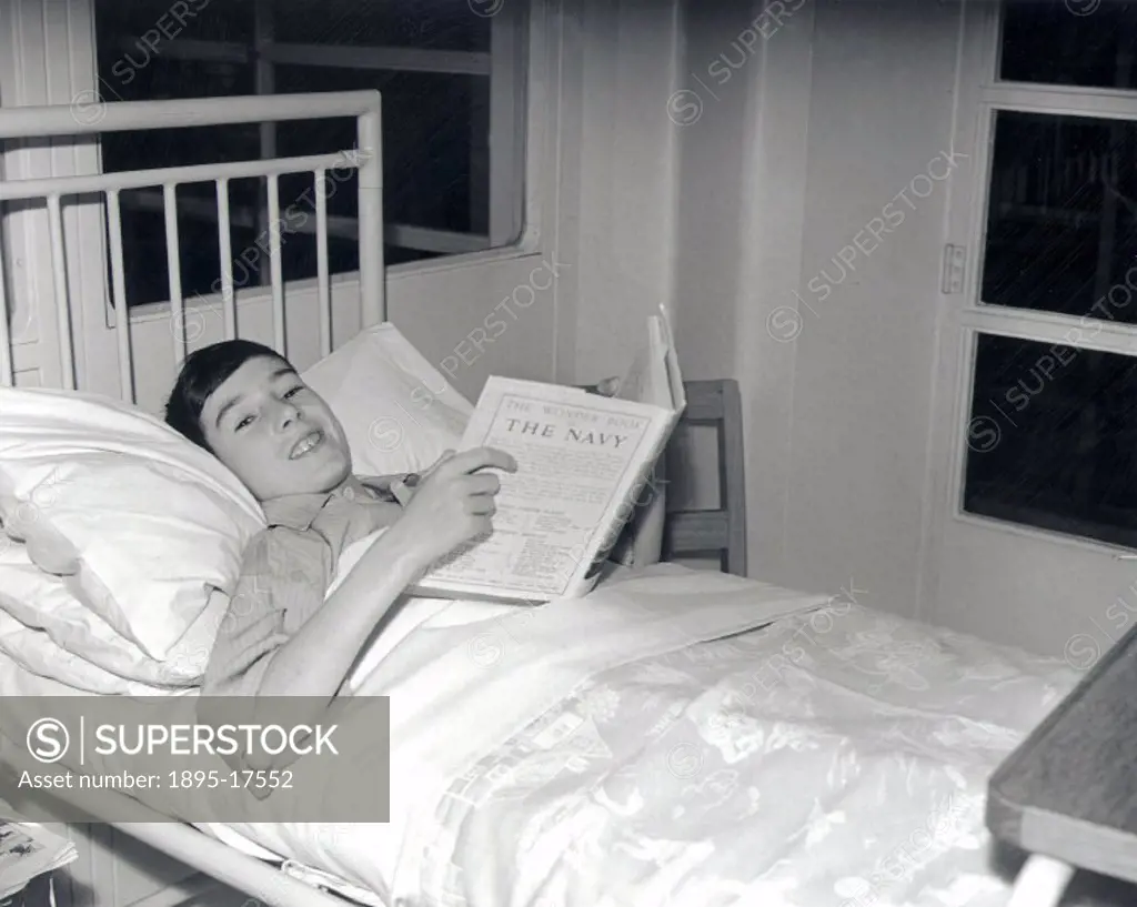 Boy in hospital bed reads book on the Navy, 23 December 1938.