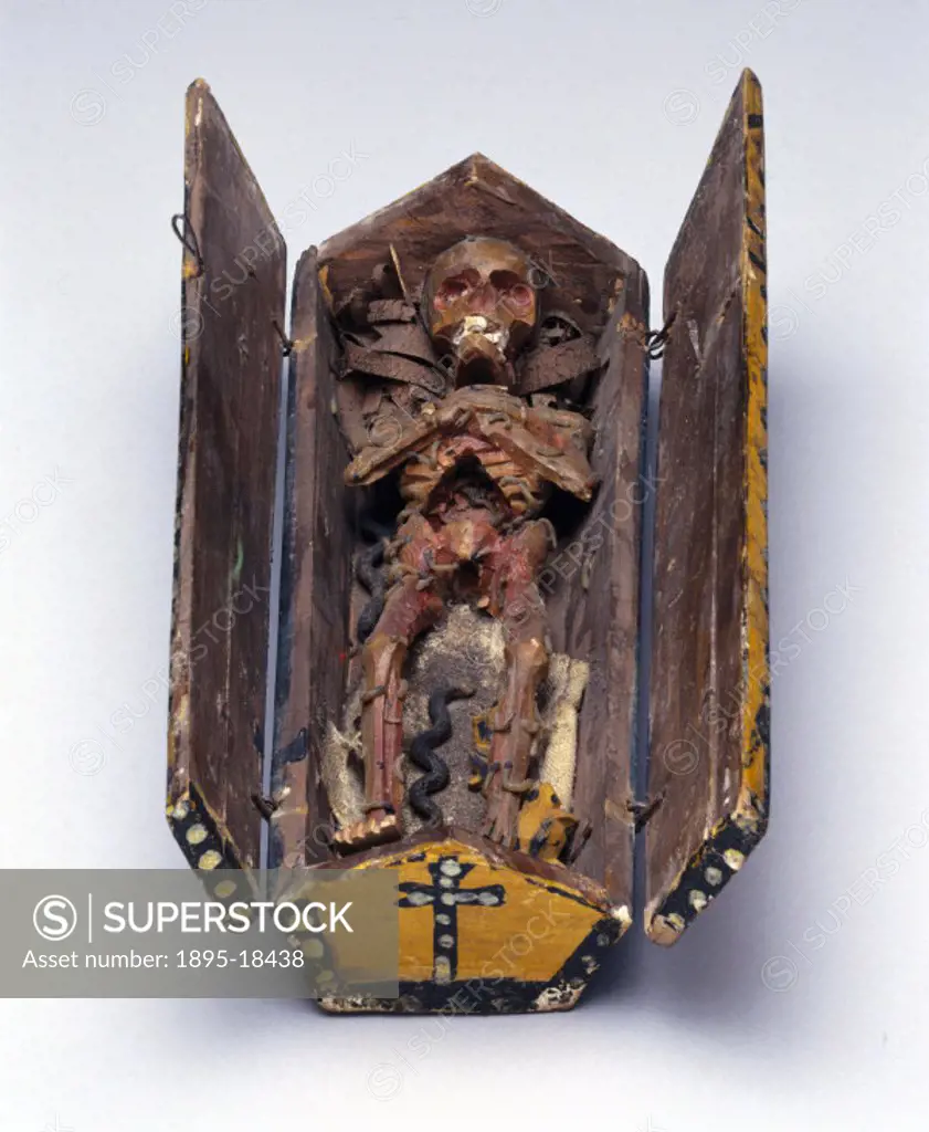 Wooden model of a stylised decomposing corpse, covered in maggots, in a wooden coffin. The coffin can be opened to reveal the corpse, as seen here.
