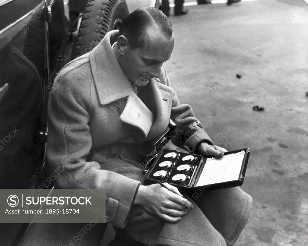 Man sitting on a running board looking at a set of stopwatches, Berlin, 1932.