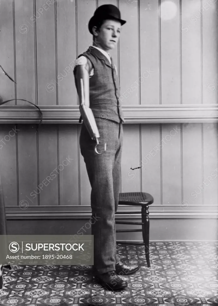 Studio photograph of a young man wearing an artificial arm. The arm was manufactured by James Gillingham (1839-1924), a boot- and shoemaker based in C...