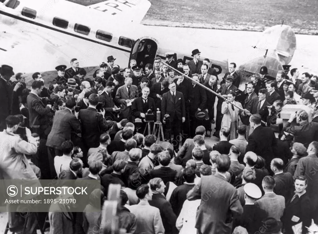 Photograph by Reuben Saidman, showing Chamberlain (1869-1940) speaking to a crowd, including members of the press, gathered beside the aeroplane he ha...