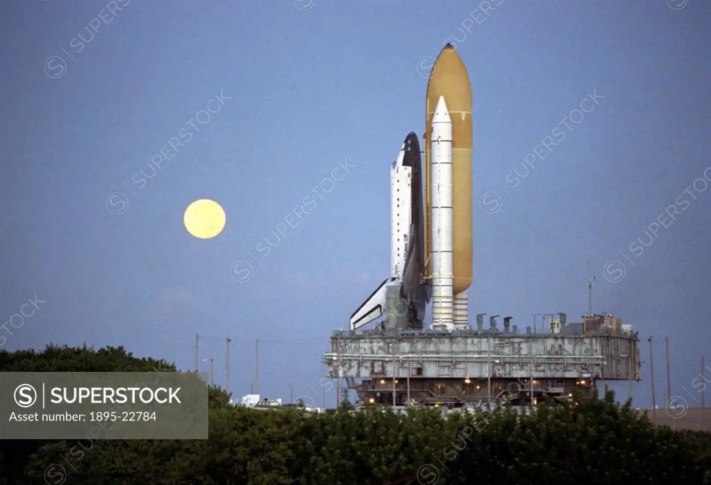 Shortly before dawn, a red-rimmed moon helps to light the way for the Space Shuttle Atlantis’ as it rolls out to launch pad 39A in preparation for la...
