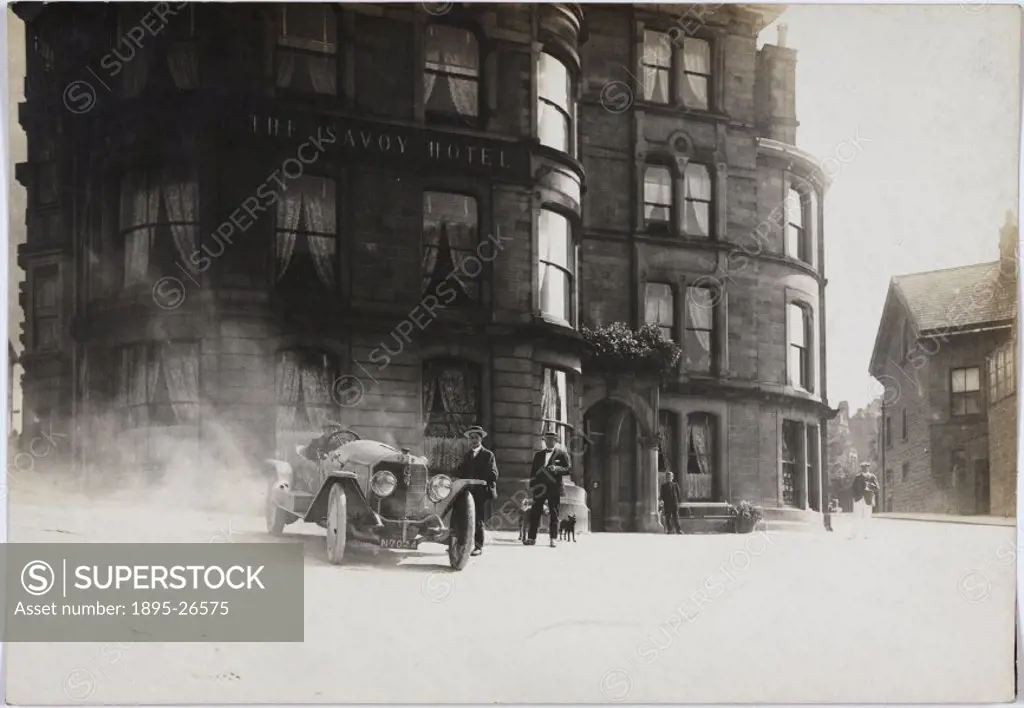 Photograph by H Wade. Two men wearing straw boaters stand beside a car parked outside a hotel called the Savoy.