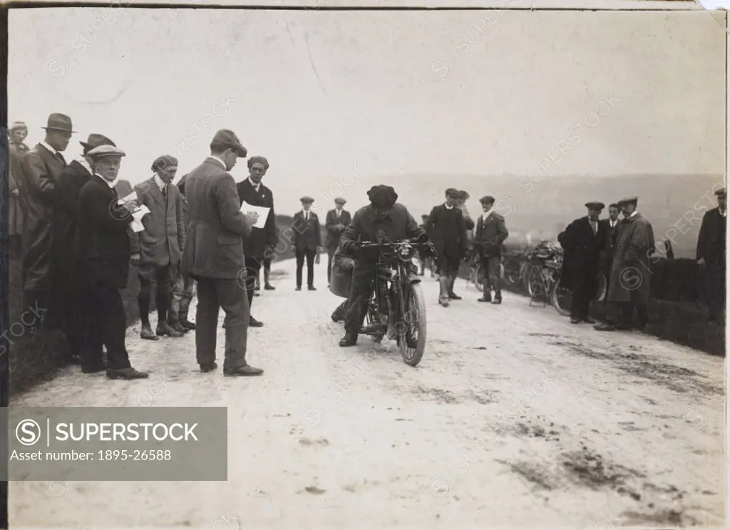 Photograph by H Wade showing a motorcycle and rider watched by officials at a trial.