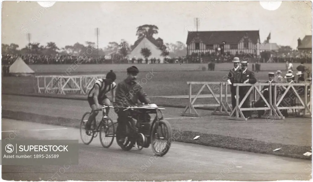 Photograph by H Wade showing a cyclist closely following a pacemaker on a motorcycle around an athletics track, watched by officials on the infield.