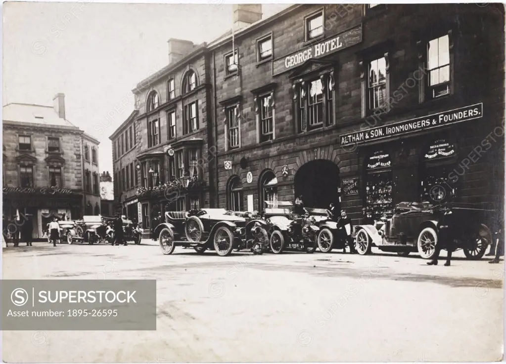 Photograph by H Wade. A street scene with several cars parked outside the George Hotel and Altham & Son, Ironmongers and Founders.