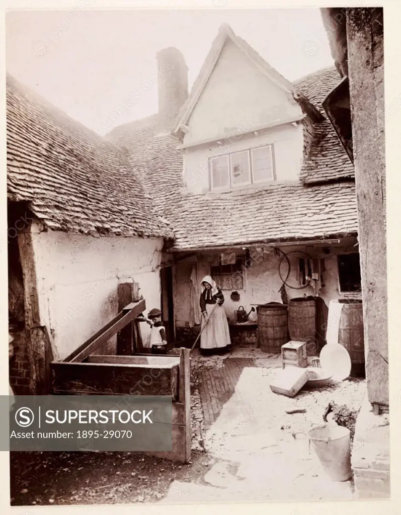 A photograph of a sunny cottage yard, taken by George Davison 1854-1930 in 1887.  A woman sweeps the steps whilst a young child operates a water pum...