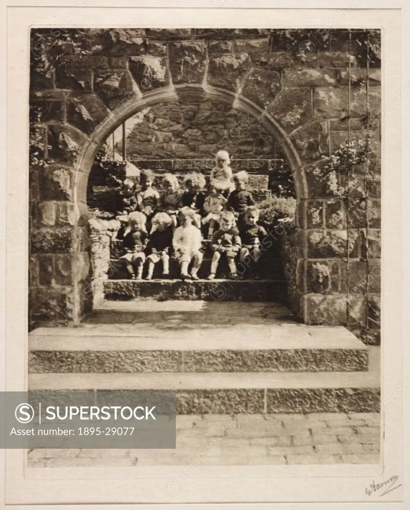 A signed photogravure of a group of children, by George Davison 1854-1930, 1913.  Twelve children sit on steps in the sunlight, framed by a stone ar...