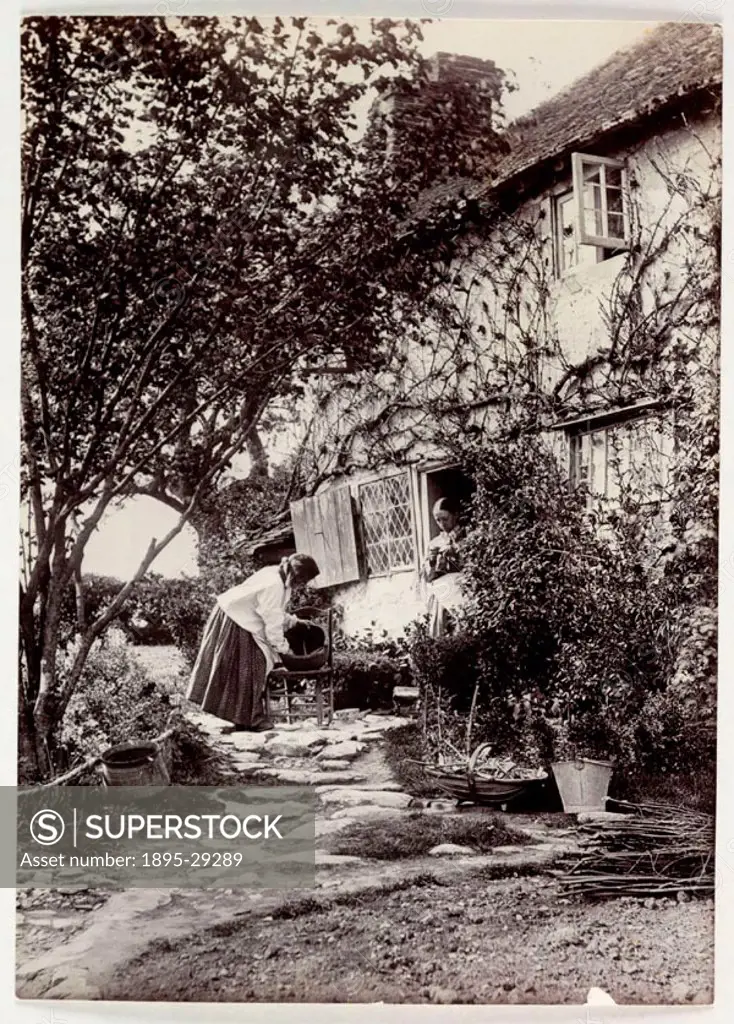 A photograph of two women in a garden, taken by Colonel Joseph Gale (c 1835-1906) about 1890. One woman stands in the doorway of the cottage sewing, t...