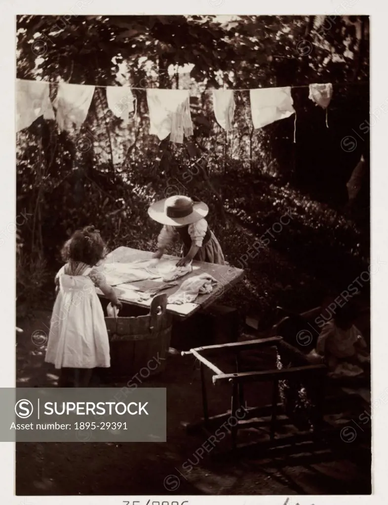 A snapshot photograph of two young girls hanging out washing to dry in a sunny garden, taken by an unknown photographer in about 1905.  Originally a s...
