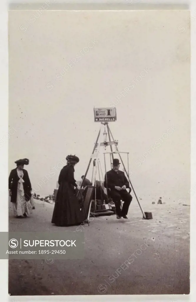 A snapshot photograph of a seaside scene, taken by an unknown photographer in about 1900.  A man sits in a weighing machine as a couple of women look ...