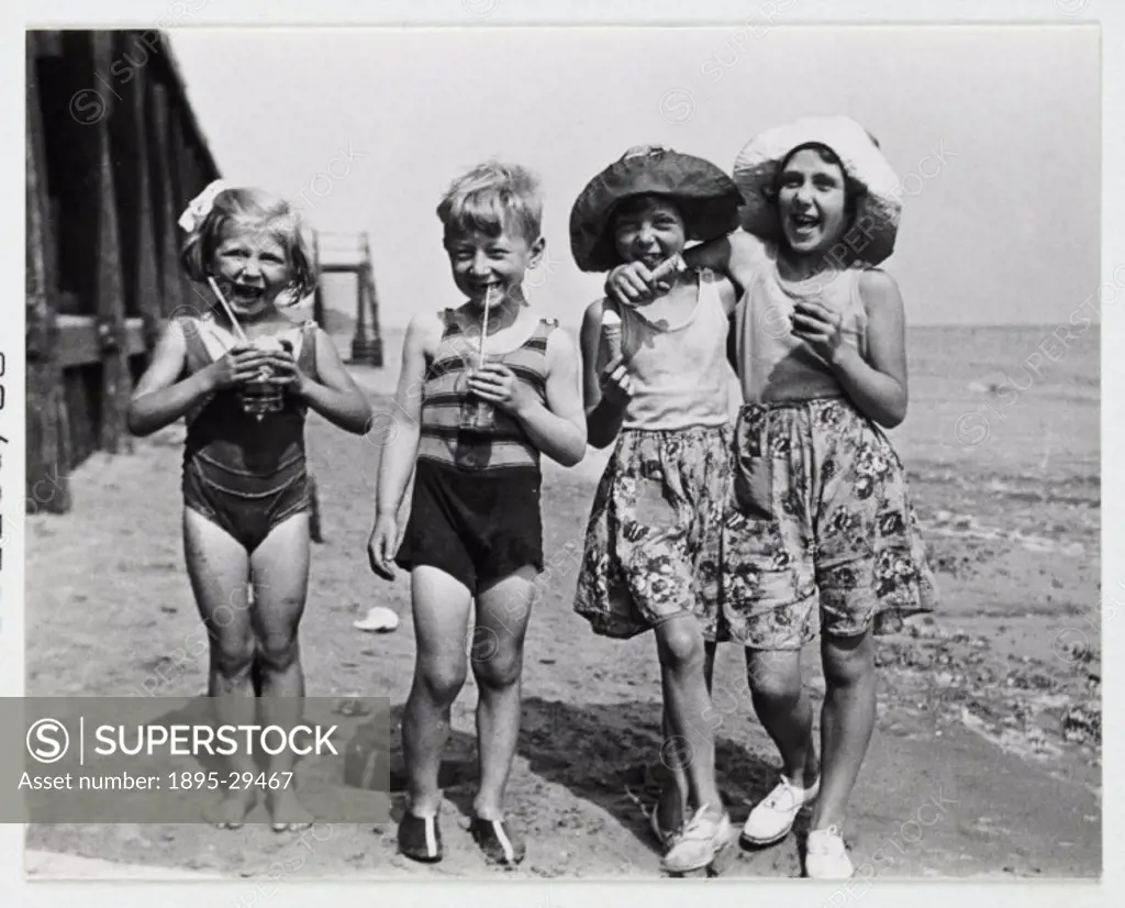 A snapshot photograph of a group of children at the seaside taken by an unknown photographer in about 1935.  A group of four laughing children stand o...