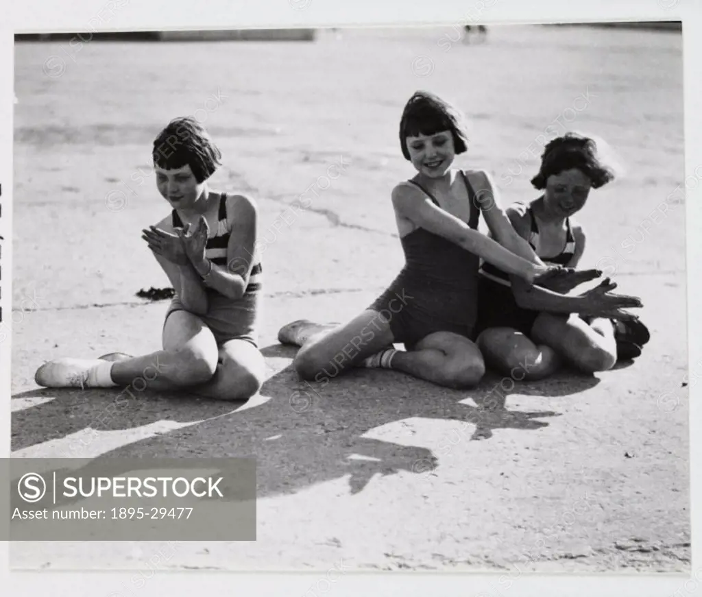 A snapshot photograph of three young girls at the seaside taken by an unknown photographer in about 1930.   Three girls, kneeling on the ground, enjoy...