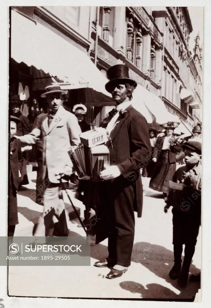 A snapshot photograph of a street musician in a busy London street, taken by an unknown photographer in about 1912.  Dressed in evening dress with a t...
