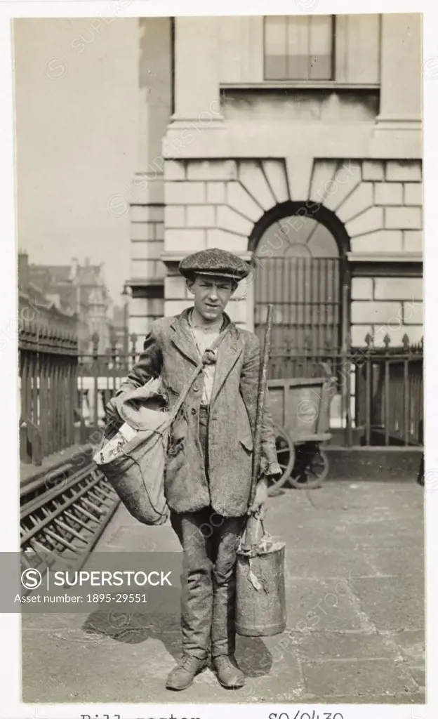A snapshot photograph of a young bill-poster, taken by an unknown photgrapher in 1915. He carries a bucket of paste, a brush and a sack of posters ove...