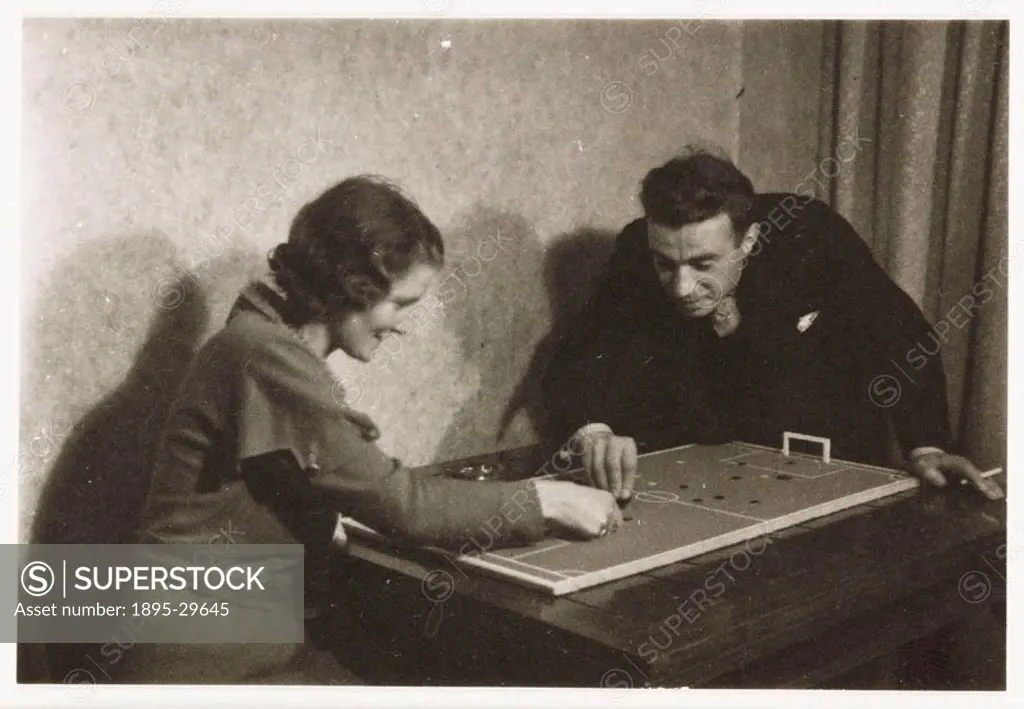 A snapshot photograph of a man and woman playing a game of table football, taken by an unknown photographer in about 1930. Originally a shooting term,...