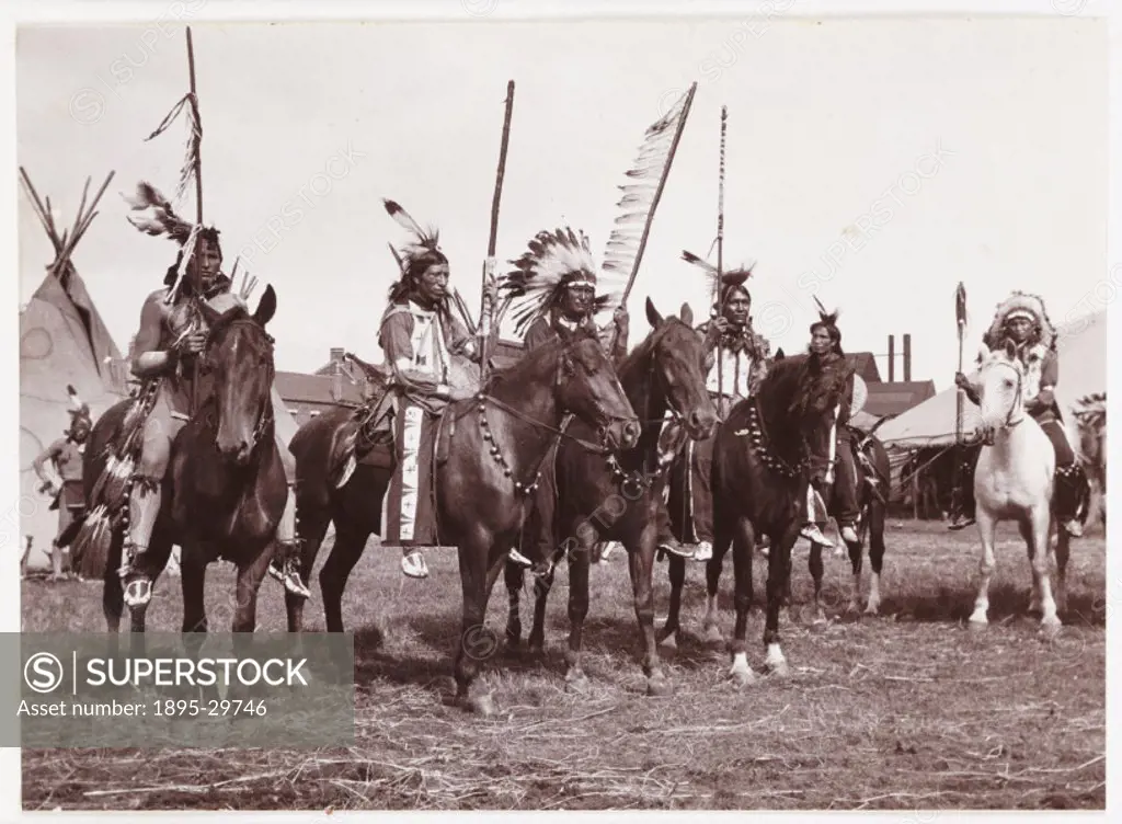 A snapshot photograph of a group of mounted Native Americans, taken by an unknown photographer in about 1905.  The factories and terraces visible behi...