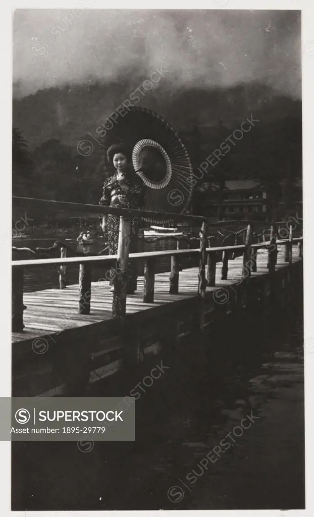 A snapshot photograph of a Japanese woman crossing a bridge, taken by an unknown photographer in about 1925.  The woman is dressed in a fine kimono an...