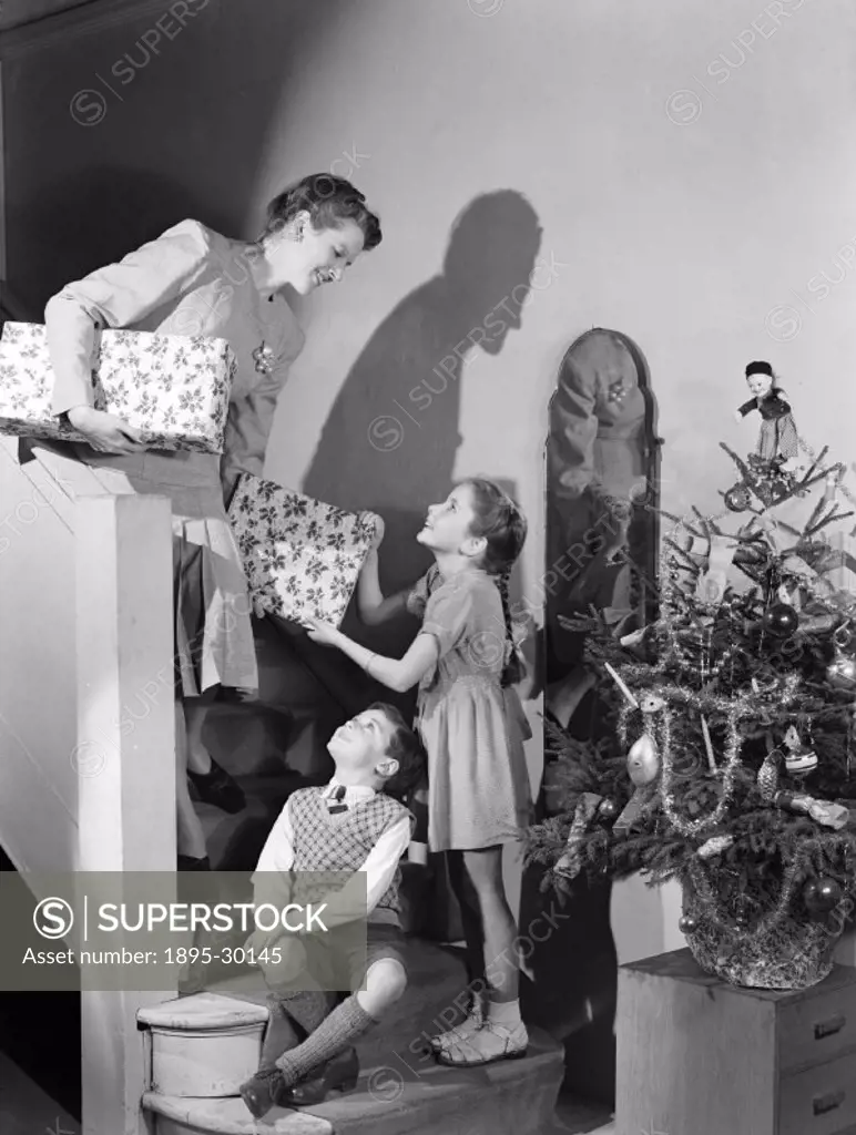 A photograph of a woman and two children on the stairs with Christmas presents, taken by Photographic Advertising Limited in about 1948. Christmas is ...