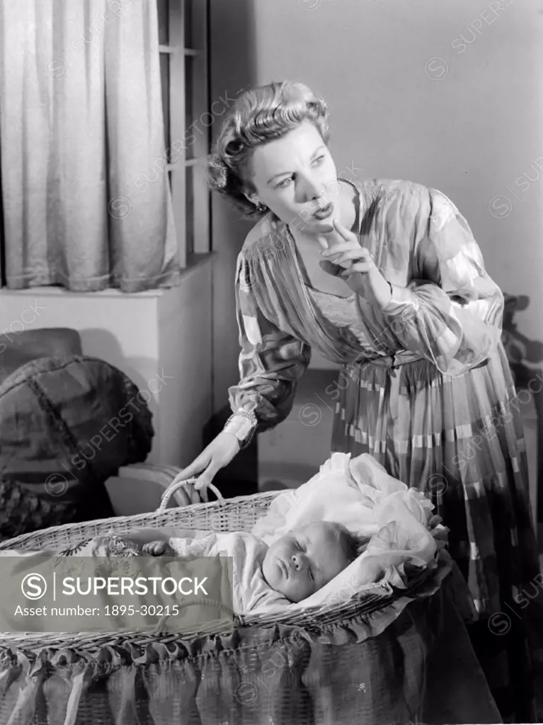 A photograph of a woman standing over a sleeping baby in a cot, taken by Photographic Advertising Limited in about 1949.  Images of children are commo...