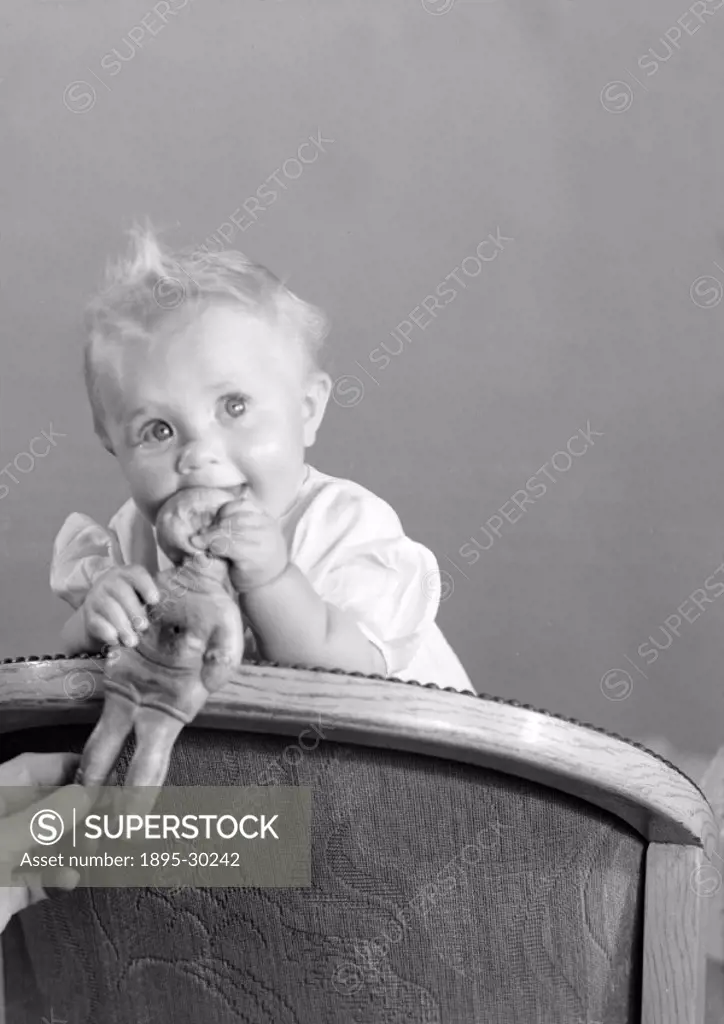 A photograph of a baby standing on a chair playing with a doll, taken by Photographic Advertising Limited took this photograph in 1950.   This photogr...