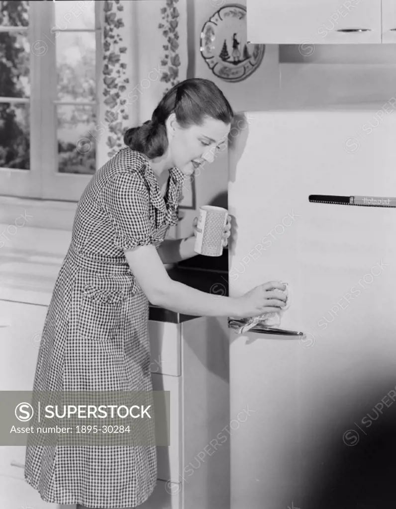 A photograph of a woman in a kitchen cleaning the door of a ´Hotpoint´ fridge, taken by Photographic Advertising Limited in about 1955.  In Britain at...